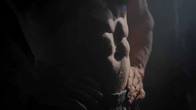 A male bodybuilder poses in shorts, showing off his muscles. Close-up of his chest and abs.