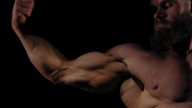 A male bodybuilder poses in shorts, showing off his arm muscles.