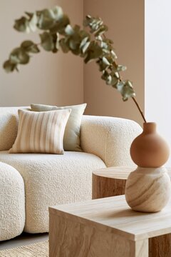 Softly blurred view through a dried eucalyptus branch, showcasing a cozy living room with a textured sofa and wooden tables in a modern interior design setting