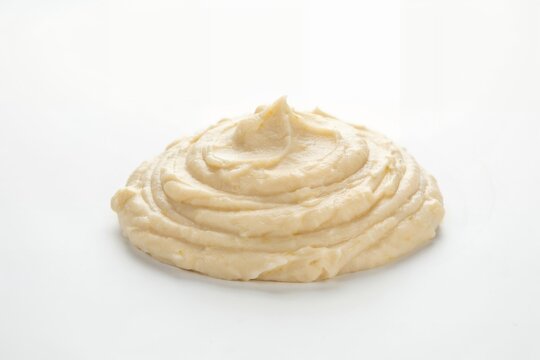 A smooth dollop of beige mashed potatoes or creamy hummus spread in a circular mound shape, isolated on a clean and plain white background