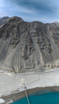 Aerial view of Keris valley featuring a winding road along the rugged mountain slopes, a turquoise river, and a bridge in Yugo, Gilgit Baltistan, Pakistan.
