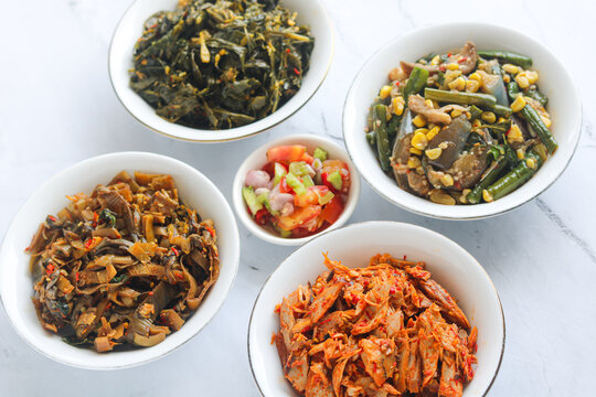 A colorful set of traditional Manado food dishes arranged neatly on round white plates.