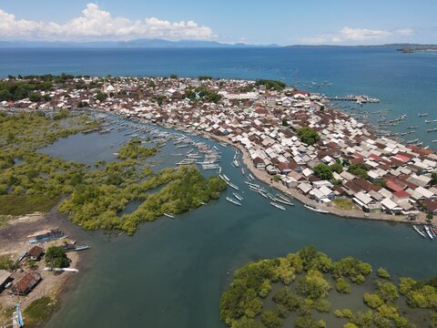 Aerial view of a coastal village on Lombok with dense housing, numerous fishing boats, and lush mangrove forests along the shoreline in Kuta Lombok, West Nusa Tenggara, Indonesia.