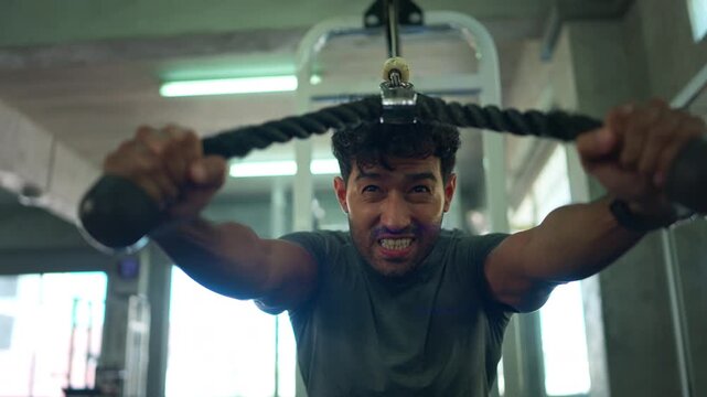 Athletic man performing a cable rope exercise to build upper body strength in a modern fitness center