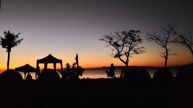 Serene seaside sunset, calm coastal scenest with twilight gradient, transitioning from deep blue at the zenith to vibrant orange and red hues near the horizon. Sea views with camping, golden hour