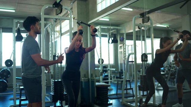 Female athlete receiving exercise guidance from a personal trainer while using a cable machine at the gym