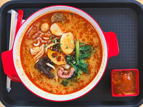 Top Down View of Spicy Chinese Malatang Hot Pot Soup with Noodles Vegetables and Meat in a Red Bowl