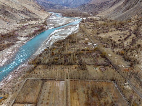 Aerial view of Ghawari village with agricultural fields, rows of poplar trees, and a turquoise river flowing through the rugged mountain valley in Ghawari, Gilgit Baltistan, Pakistan.