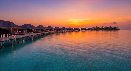 Obraz premium A stunning overwater bungalow resort stretches along a turquoise lagoon at sunset.