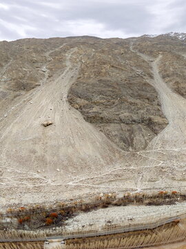 Aerial view of rugged, arid mountain slopes, steep scree, rocky terrain, and a valley floor with sparse vegetation in Ghawari, Gilgit Baltistan, Pakistan.