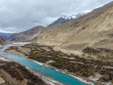 Aerial view of the Shyok River flowing through the rugged valley with snow-capped peaks, sparse vegetation, and rocky mountain slopes in Ghawari, Gilgit Baltistan, Pakistan.