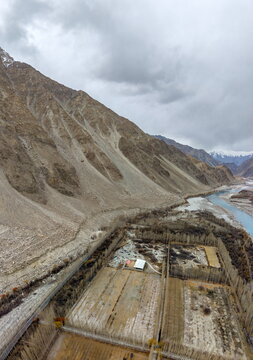 Aerial view of agricultural fields and a river winding through the rugged mountain landscape of Ghawari, with rows of trees and rocky slopes in Ghawari, Gilgit Baltistan, Pakistan.