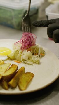 Vertical video. Dinner preparation. Restaurant culinary. Chef hand adding sliced onion to served hot dish. Appetizing lunch potato egg sausage on plate.