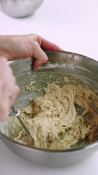 Vertical video. Confectionery process. Mixing dough. Baker hand stirring flour mass in stainless steel bowl with professional tool.
