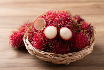 Fototapeta premium Fresh rambutan fruit in a wicker basket on wooden background, Tropical summer fruit in Thailand