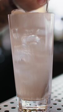 Vertical video. Stirring cocktail. Cold cream drink. Barman preparing ice cube water with whipped milk. Tall glass sweet flavored beverage.