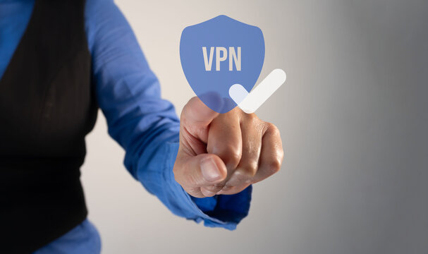 Hand taps glowing VPN shield icon. Person wears blue shirt and black vest. Action suggests secure online connection. Suitable for tech, cybersecurity, and privacy themes