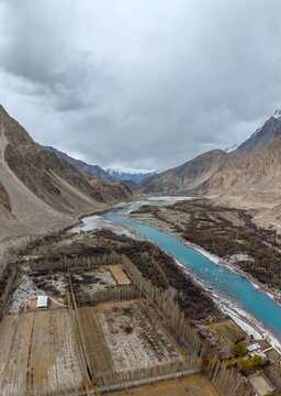 Aerial view of Ghawari valley featuring a turquoise river flowing through agricultural fields and rows of trees surrounded by mountains in Ghawari, Gilgit Baltistan, Pakistan.