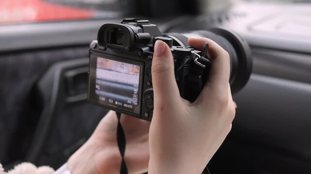 Hands hold camera inside car, filming through window. Focus on lens and screen, capturing outdoor view. Calm, focused mood as person records surroundings. Ideal for travel, vlogging