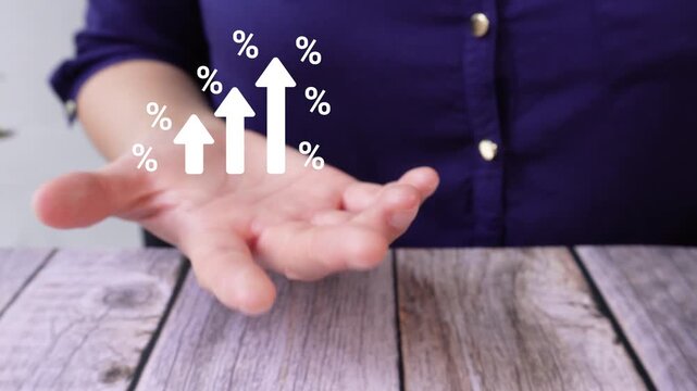 Close-up of a woman's hand on a table holding an animated chart with rising arrows surrounded by percentage symbols. Ideal for tables, reports, or financial visual representations.