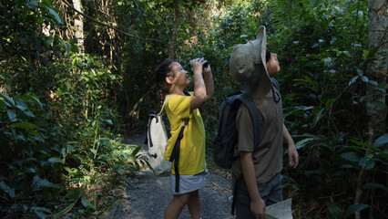 Obraz premium Two Asian Children Using Binoculars While Hiking in Tropical Forest