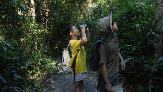 Two Asian Children Using Binoculars While Hiking in Tropical Forest