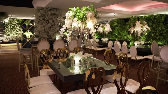 Stabilized camera shot focusing on an elegant mirror table with glowing candle reflections, a silver floral candelabra, and premium gold back chairs.