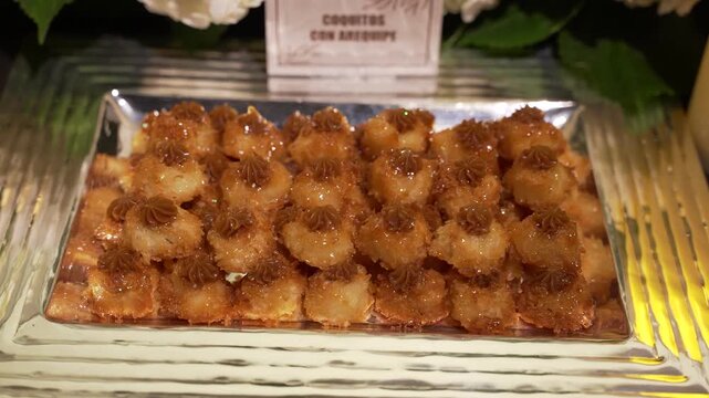 Close-up of gourmet bite-sized desserts presented on an elegant serving tray during a luxury wedding reception, gala or special event. Sophisticated catering presentation with floral decorations