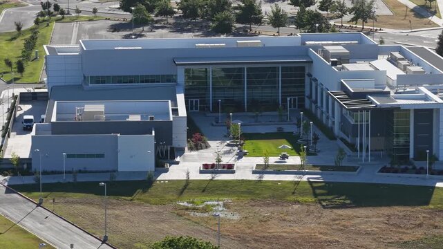 Modern architecture of Clovis Community College in Fresno, California, featuring contemporary buildings, a central courtyard with green lawn, and surrounding parking lots filmed from a drone