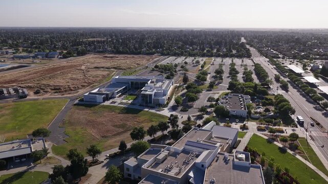 Sweeping aerial view of the Clovis Community College campus in Fresno, California, showing modern architecture, green lawns, an expansive parking lot, and the surrounding suburban landscape