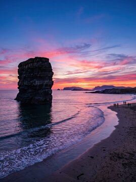 Dramatic coastal sea stack at sunset, vibrant pink and purple sky over ocean beach, scenic vertical landscape for travel and nature backgrounds