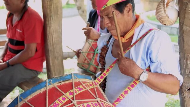 Lamas, Tarapoto/Peru - March 17, 2024: Traditional drumming ceremony in rustic wooden shelter. Old man plays vibrant, handcrafted drum with focused expression. Younger participants sit nearby, listeni