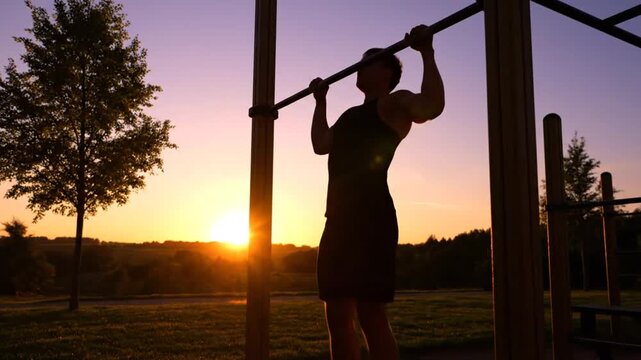 silhouette of athletic man doing pull-ups on horizontal bar at outdoor park during beautiful sunset