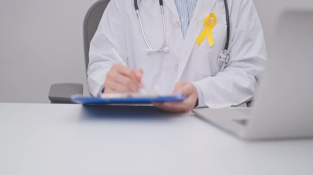 Professional doctor using laptop and taking report notes on notebook for Yellow Ribbon concept of yellow September, Suicide prevention day, Childhood, July Sarcoma, bone and bladder cancer