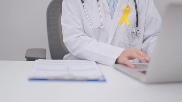 Professional doctor using laptop and taking report notes on notebook for Yellow Ribbon concept of yellow September, Suicide prevention day, Childhood, July Sarcoma, bone and bladder cancer