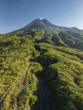 Aerial view of the lush green slopes of Mount Merapi volcano with a deep ravine and rocky path in Sleman Regency, Special Region of Yogyakarta, Indonesia.
