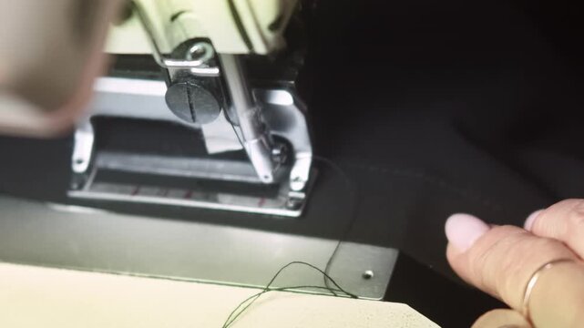 Apparel making. Tailoring process. Female hand stitching garment button hole on black clothing on electrical equipment in workshop.