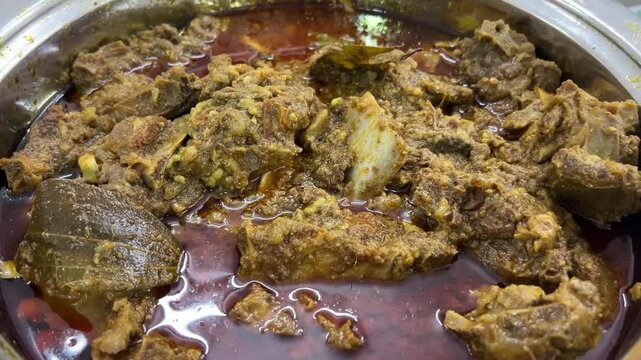 A steaming bowl of rich, slow-cooked spicy mutton curry, glistening with aromatic oils and traditional regional spices, India.