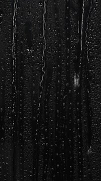 water drops flow down the surface of glass on black background.	