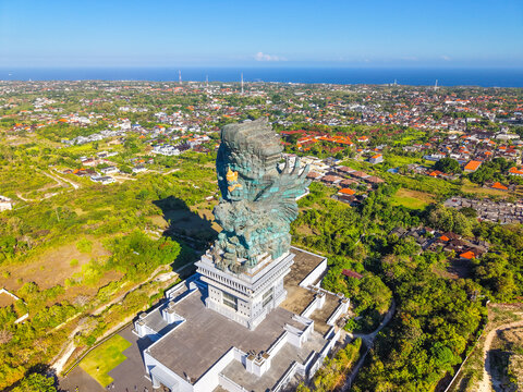 A dramatic drone angle frames the golden-crowned figure of Vishnu astride the outstretched wings of Garuda, the mythical eagle of Hindu cosmology, rendered in monumental oxidised bronze above Bali.