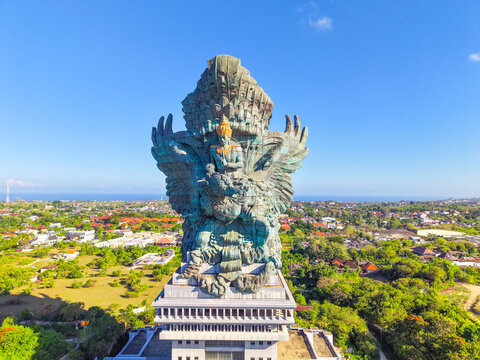 The towering silhouette of the Garuda Wisnu Kencana statue presides over the Bukit Peninsula with the shimmering expanse of the Indian Ocean visible along the horizon in the warm afternoon light.