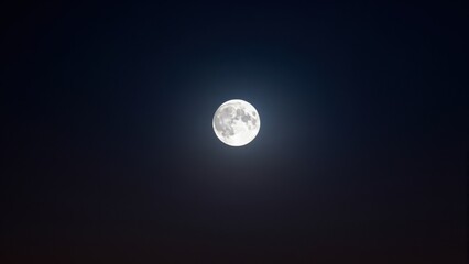 Obraz premium Full Moon in Dark Sky: A bright, luminous full moon hangs in the vast, deep blue twilight sky, casting a serene and mysterious glow.