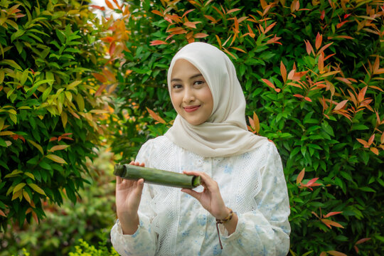 A young Asian Muslim woman is enjoying getuk pisang, a specialty food from Kediri, Indonesia, made from mashed steamed bananas wrapped in banana leaves.