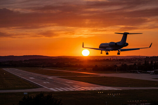Private jet aircraft approaching a runway for landing during a deep orange sunset