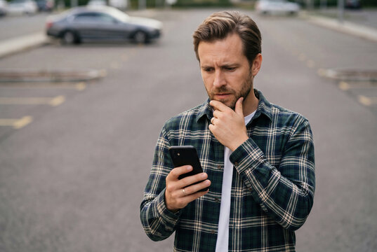 Thoughtful man looking at his smartphone in a parking lot