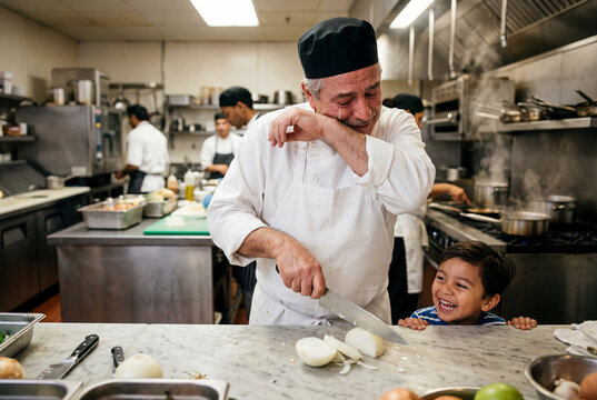 Older male chef wiping tears while chopping onions next to child