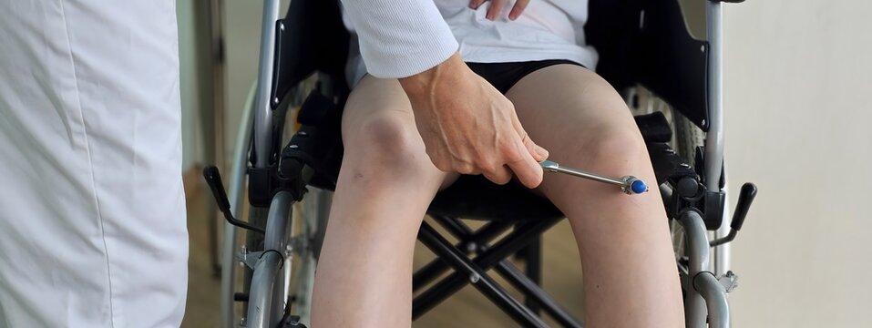 Healthcare professional performs a reflex test on a patient in a wheelchair during a routine examination