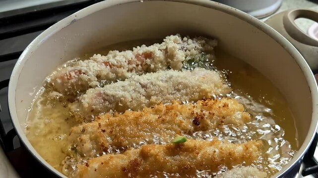 Breaded chicken cutlets sizzle in a pot of hot oil as they fry to a crisp golden brown at home.