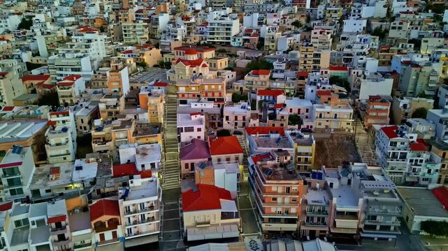 Compact urban neighborhood of mid-rise apartments with red roofs fills the frame as the drone glides overhead at dusk.