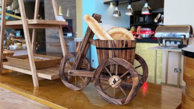 A rustic wooden tricycle cart displays fresh baked bread and baguettes on a polished counter. The static food display sits inside a brightly lit indoor hotel buffet catering area.